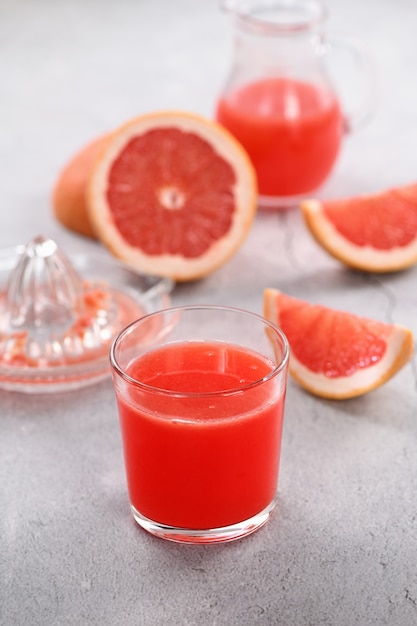 Um copo de suco de toranja feito na hora e fatias de frutas frescas em um fundo claro de concreto