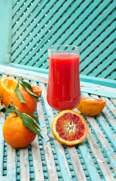 Foto um copo de suco fresco de laranjas sanguíneas em uma superfície verde velha. laranjas ao fundo