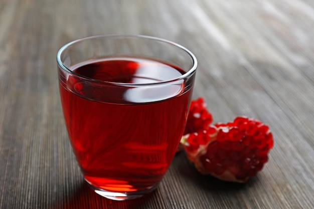 Um copo de suco saboroso e frutas granadas em fundo de madeira