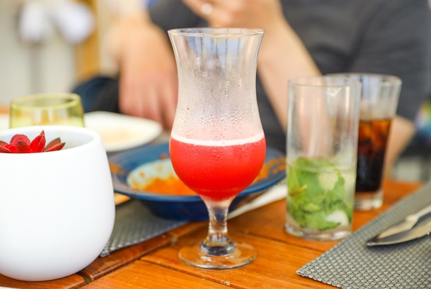 Um copo de suco vermelho está sobre uma mesa com outras bebidas.