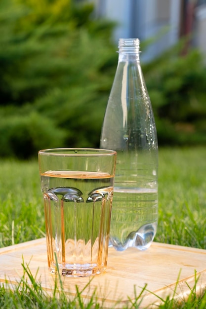 um copo de vidro com água ao lado de uma garrafa de plástico está no jardim na grama verde