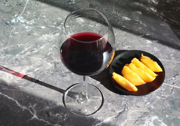 Um copo de vinho tinto seco fica sobre uma mesa de mármore atrás de pêssegos fatiados