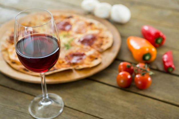 Um copo de vinho tinto servido com pizza italiana no fundo