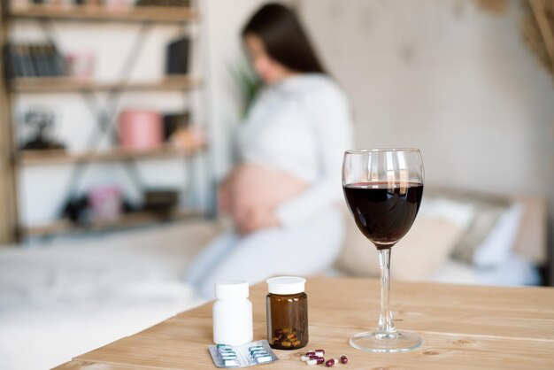 Foto um copo de vinho vermelho e comprimidos no fundo de uma mulher grávida conceito alcoólico.