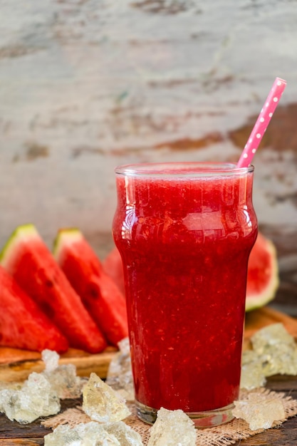 Um copo grande com um smoothie de melancia frio e alguns triângulos de melancia como fundo