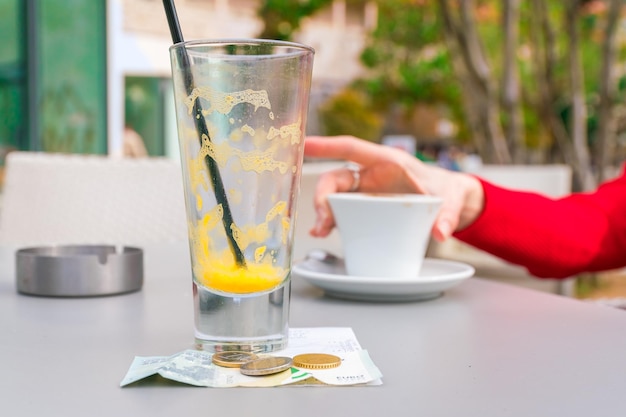 Foto um copo vazio de sumo de laranja e dinheiro numa mesa num café.