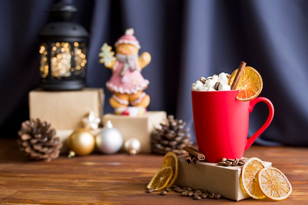 Um copo vermelho fosco com marshmallows e canela em um fundo de Natal