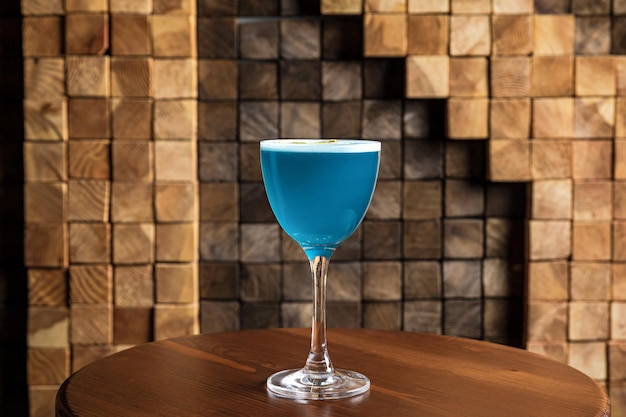 Um coquetel alcoólico azul azedo em um copo de entalhe e nora em uma mesa de madeira no bar e espaço de cópia de fundo de madeira