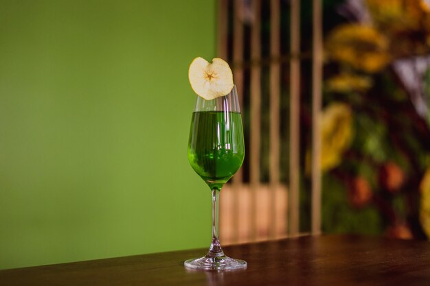 Um coquetel verde em um copo de flauta decorado com uma fatia de maçã desidratada