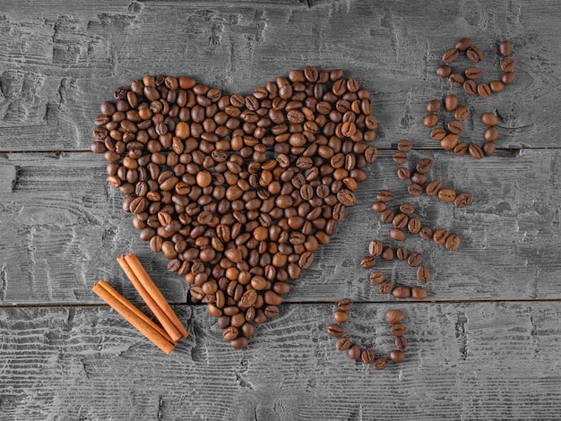 Um coração de grãos de café e dois paus de canela em uma mesa de madeira preta. A vista do topo. Grãos para a preparação da bebida popular.