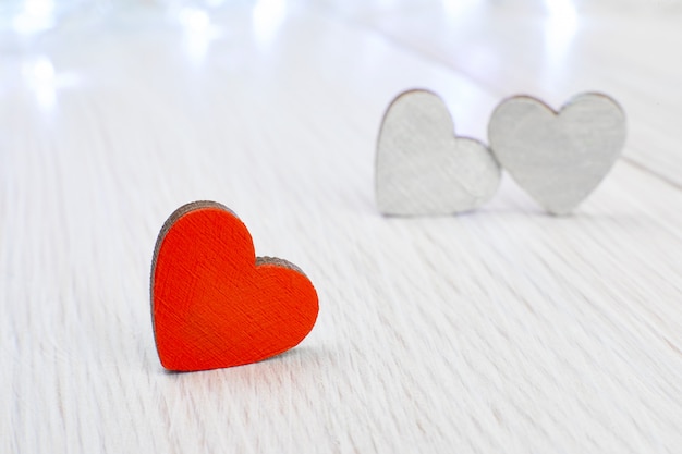 Um coração de madeira vermelho em oposição a dois cinzas em uma luz de madeira. A concepção de amor não correspondido, azarado dia dos namorados