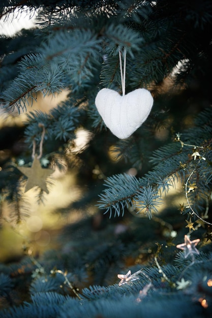 Um coração de malha macio paira sobre os galhos de uma árvore de natal decorada na temporada de férias