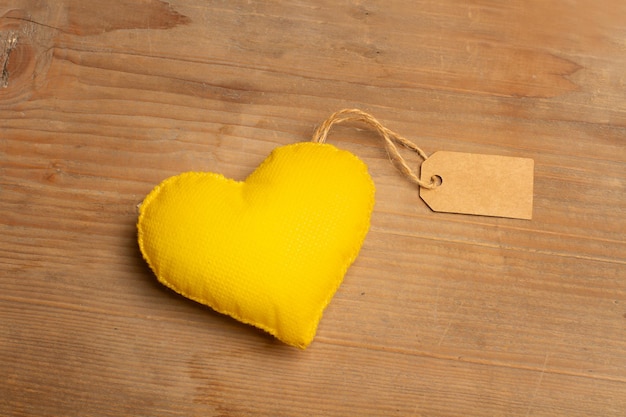 Um coração de tecido amarelo com uma etiqueta de papelão em um fundo de madeira com espaço de cópia