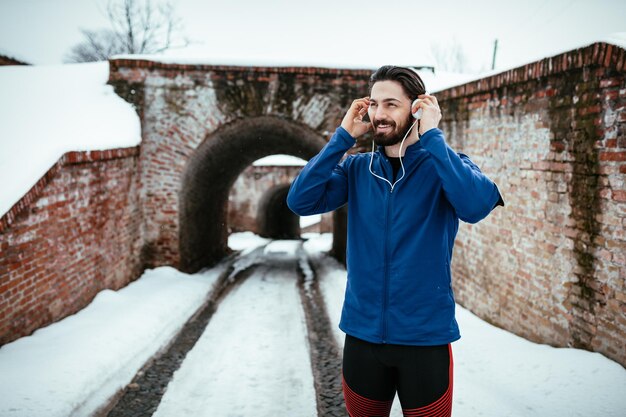 Um corredor masculino usando fones de ouvido e se preparando para correr em local público durante o treinamento de inverno do lado de fora. Copie o espaço.