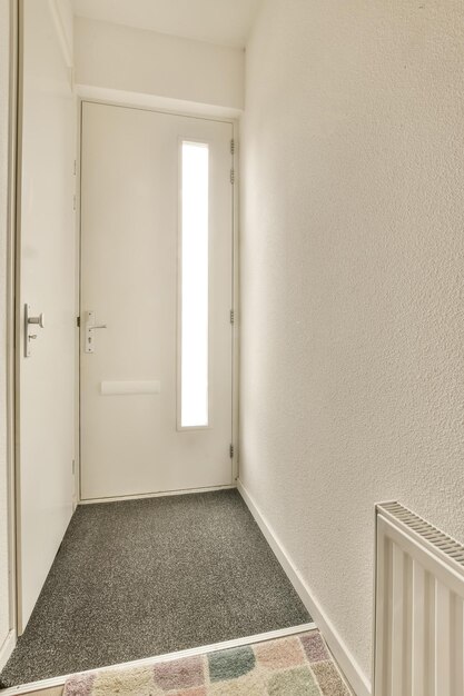 Um corredor vazio com paredes brancas e carpete preto há uma porta que leva à entrada da sala