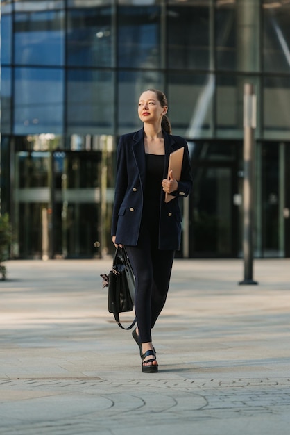 Um corretor de imóveis feminino em um blazer está andando com um laptop entre arranha-céus