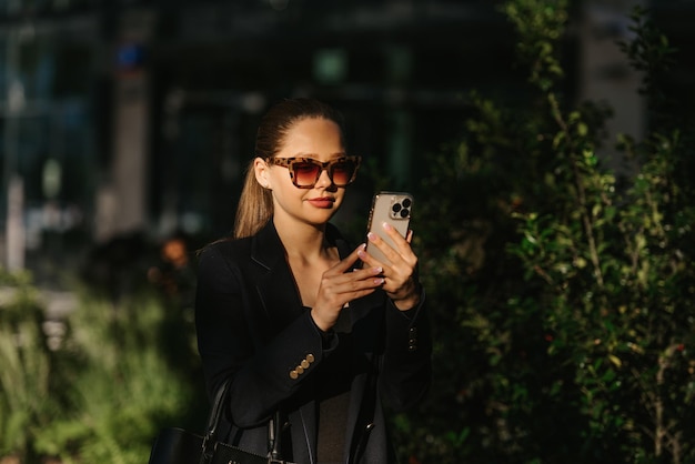 Um corretor de imóveis feminino em um blazer está segurando um telefone no jardim moderno ao pôr do sol