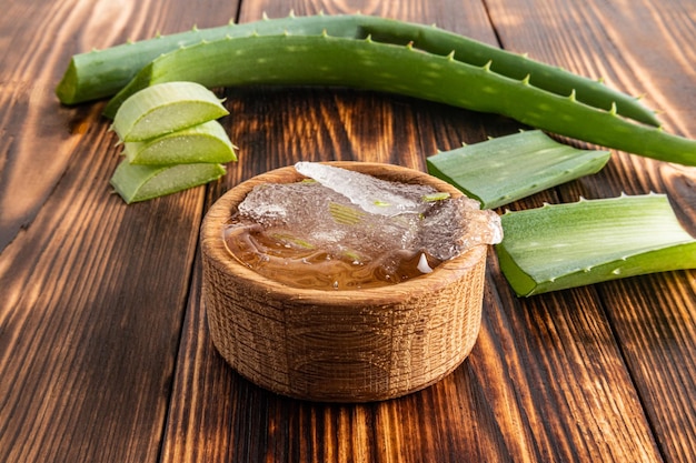 Um corte da polpa de aloe vera em uma tigela de madeira em uma mesa de aldeia entre as folhas vista frontal o conceito de preparar o gel em casa