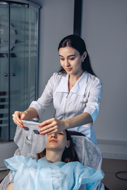 Um cosmetologista faz uma máscara de tecido com colágeno para um jovem cliente em um salão de spa para considerações sobre a qualidade da pele facial.