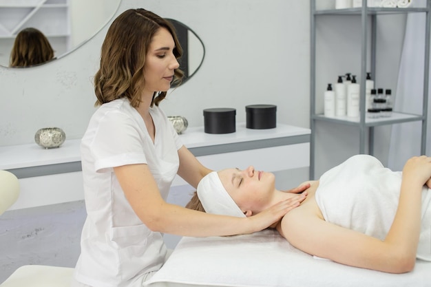 Um cosmetologista massageia a área do colarinho A garota está deitada com os olhos fechados