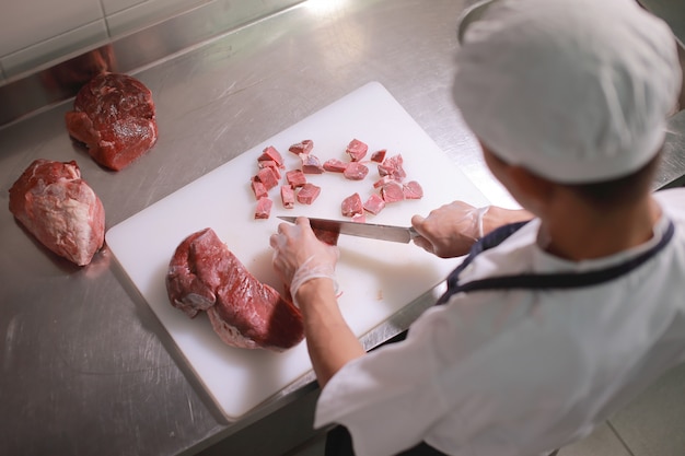 Um cozinheiro corta a carne crua na mesa da cozinha.