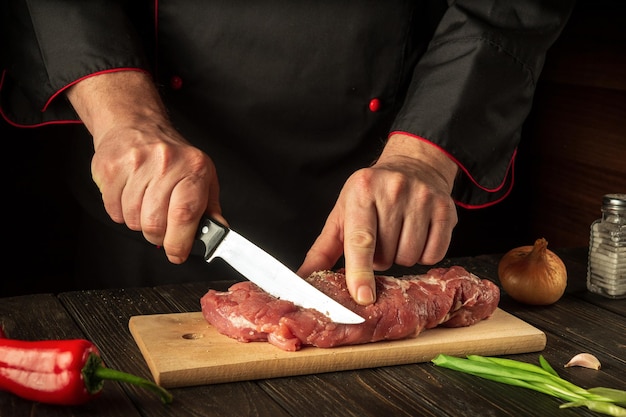 Um cozinheiro corta vitela crua em uma tábua de corte com uma faca antes de cozinhar cozinha asiática ideia de receita de hotel