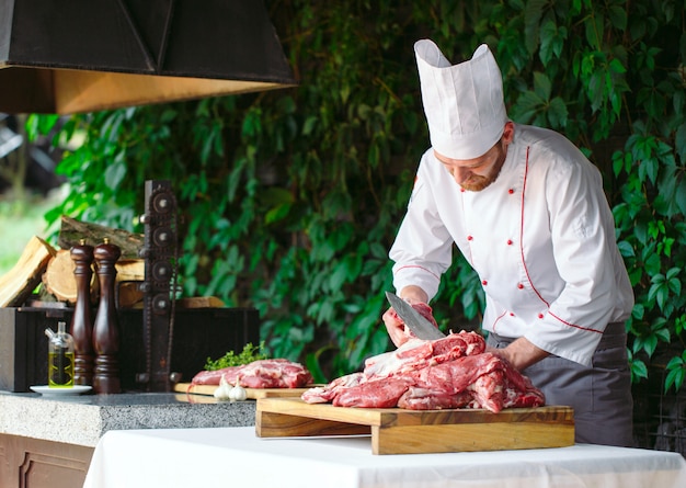Um cozinheiro de homem corta carne com uma faca em um restaurante.