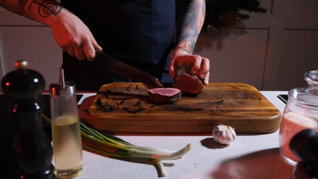 Um cozinheiro em uma tábua de madeira corta um bife frito em pedaços grandes em close-up