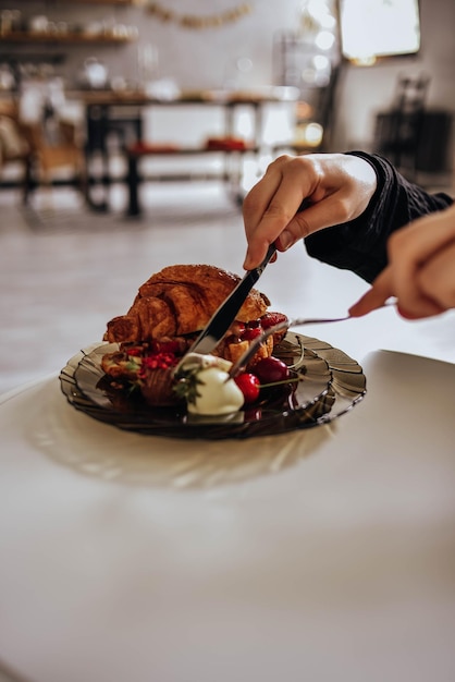 Foto um croissant francês com morangos está em um prato que uma mulher corta