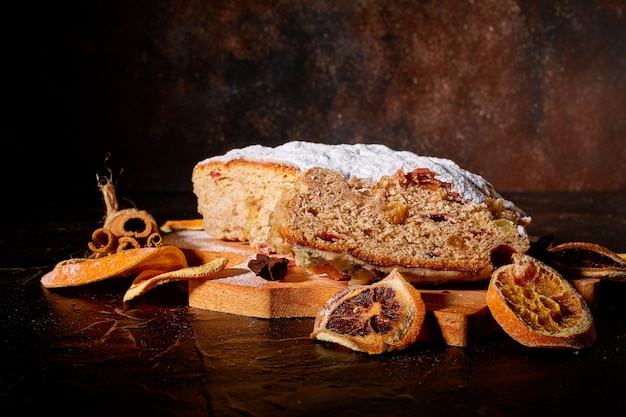 Um delicioso bolo doce polvilhado com açúcar em pó está rodeado por laranjas secas e canela e uma tábua de madeira