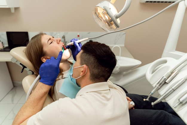 Foto um dentista altamente qualificado trata os dentes de um paciente jovem tratamento odontológico sem dor dentista de tratamento odontológico moderno examina dentes problemáticos