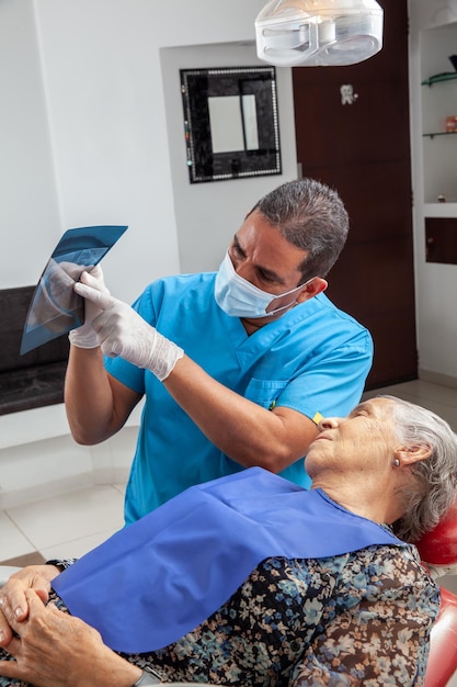 Foto um dentista de meia-idade usa uma imagem de raios-x para explicar o tratamento à sua paciente idosa