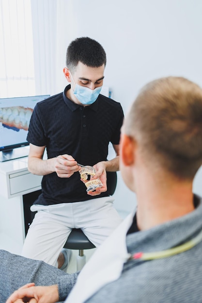 Um dentista em um consultório odontológico moderno conta a um paciente sobre cuidados dentários Um homem se senta em uma cadeira odontológica e ouve um dentista