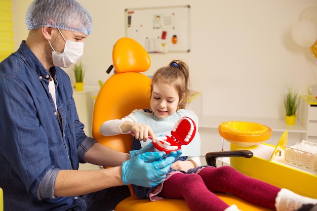 Um dentista masculino ensina uma garotinha a escovar os dentes corretamente com uma escova de dentes