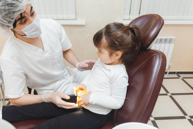 Um dentista masculino mostra a uma garota em uma dentadura como escovar os dentes corretamente o conceito de exame médico infantil