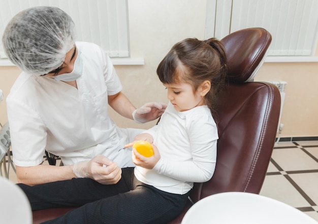 Um dentista masculino mostra a uma garota em uma dentadura como escovar os dentes corretamente o conceito de exame médico infantil