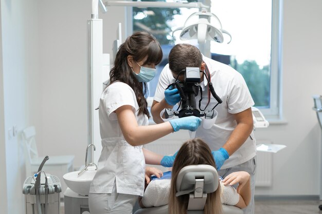 Um dentista trabalhando e uma enfermeira tratando os dentes de uma mulher sentada em uma cadeira. Os ortodontistas trabalham com próteses. Copie o espaço. Medicina oral e conceito de saúde.