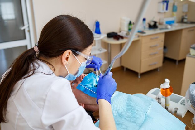 Um dentista trata um paciente do sexo masculino com instrumentos odontológicos. O dentista examina os dentes dos pacientes na clínica odontológica. Foco seletivo