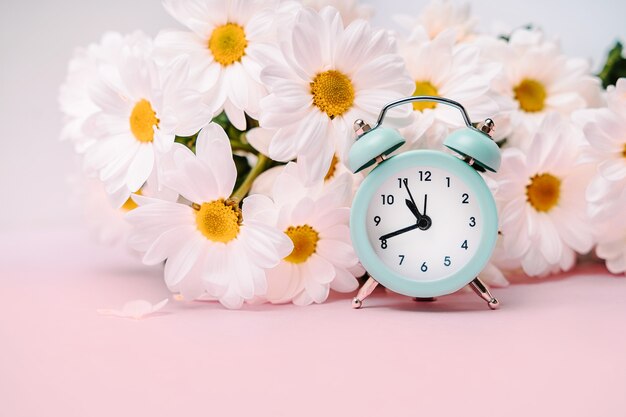 Um despertador azul suave em um buquê de margaridas. Conceito floral para férias