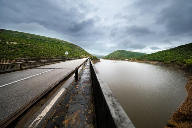 Um dia chuvoso de outono, uma estrada solitária serpenteia perto de uma paisagem serena de reservatório.