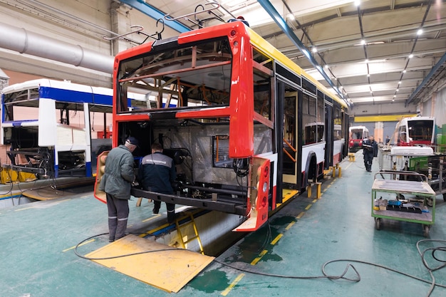 Um dia útil de fabricação de ônibus automático moderno com trabalhadores de carros inacabados em fundo de peças automotivas uniformes de proteção