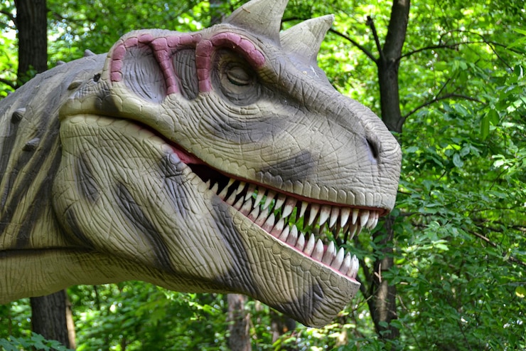 Foto um dinossauro com a boca aberta se posiciona contra o pano de fundo de uma densa floresta verde lagartos extintos