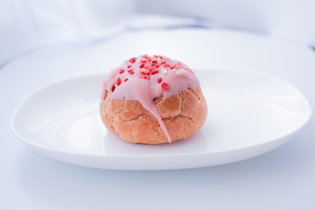 Um donut com glacê rosa e granulado por cima está em um prato.