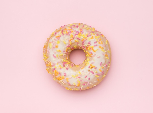 Um donut de vidro claro polvilhado com decorações doces em um fundo rosa o conceito mínimo de panificação popular