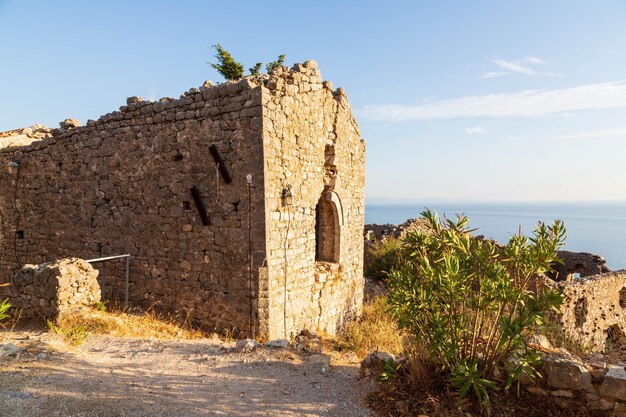 Um edifício de pedra na encosta de uma colina com o mar ao fundo.