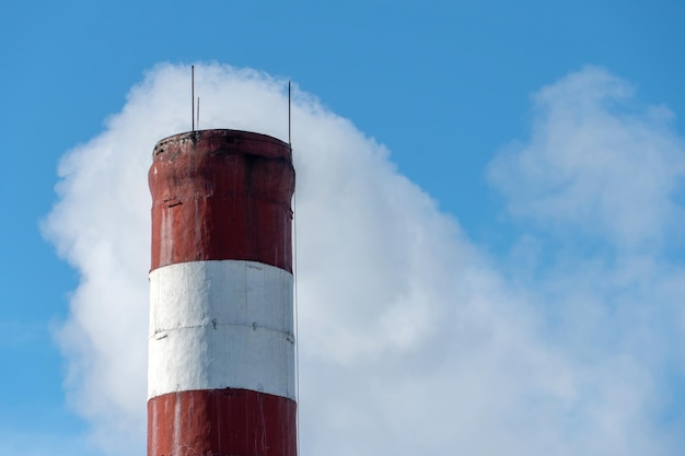 Um edifício industrial e uma chaminé com fumaça branca contra um céu azul Poluição do ar pela fumaça de uma fábrica em funcionamento Indústria química e o risco de desastre ambiental