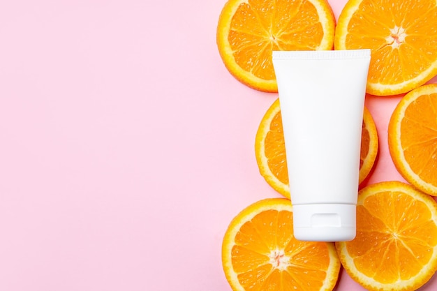 Um elegante tubo cosmético branco é artisticamente colocado entre fatias de laranja vibrantes em um rosa suave