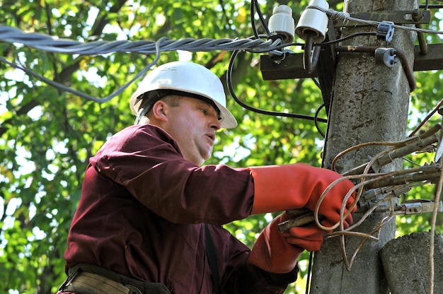 Um eletricista em um poste elétrico repara fios em uma linha de energia