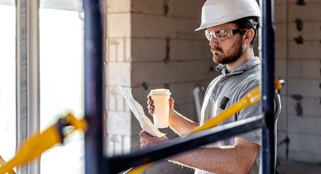 Um eletricista estuda um desenho de construção com um café na mão.