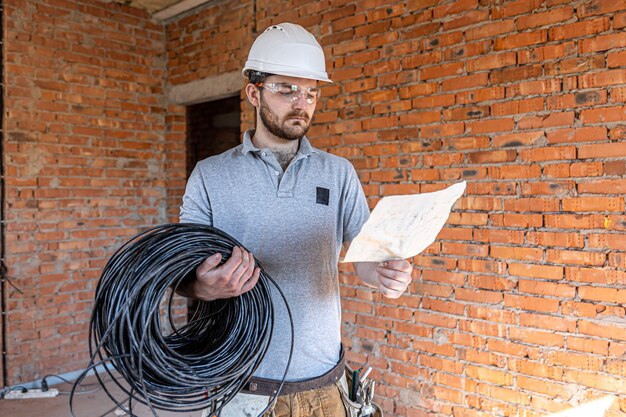 Um eletricista examina um desenho de construção enquanto segura um cabo elétrico na mão em um local de trabalho